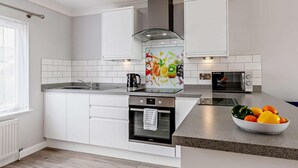 Een moderne keuken met witte kastjes, een roestvrijstalen oven, een magnetron, en een schaal fruit op het aanrecht.