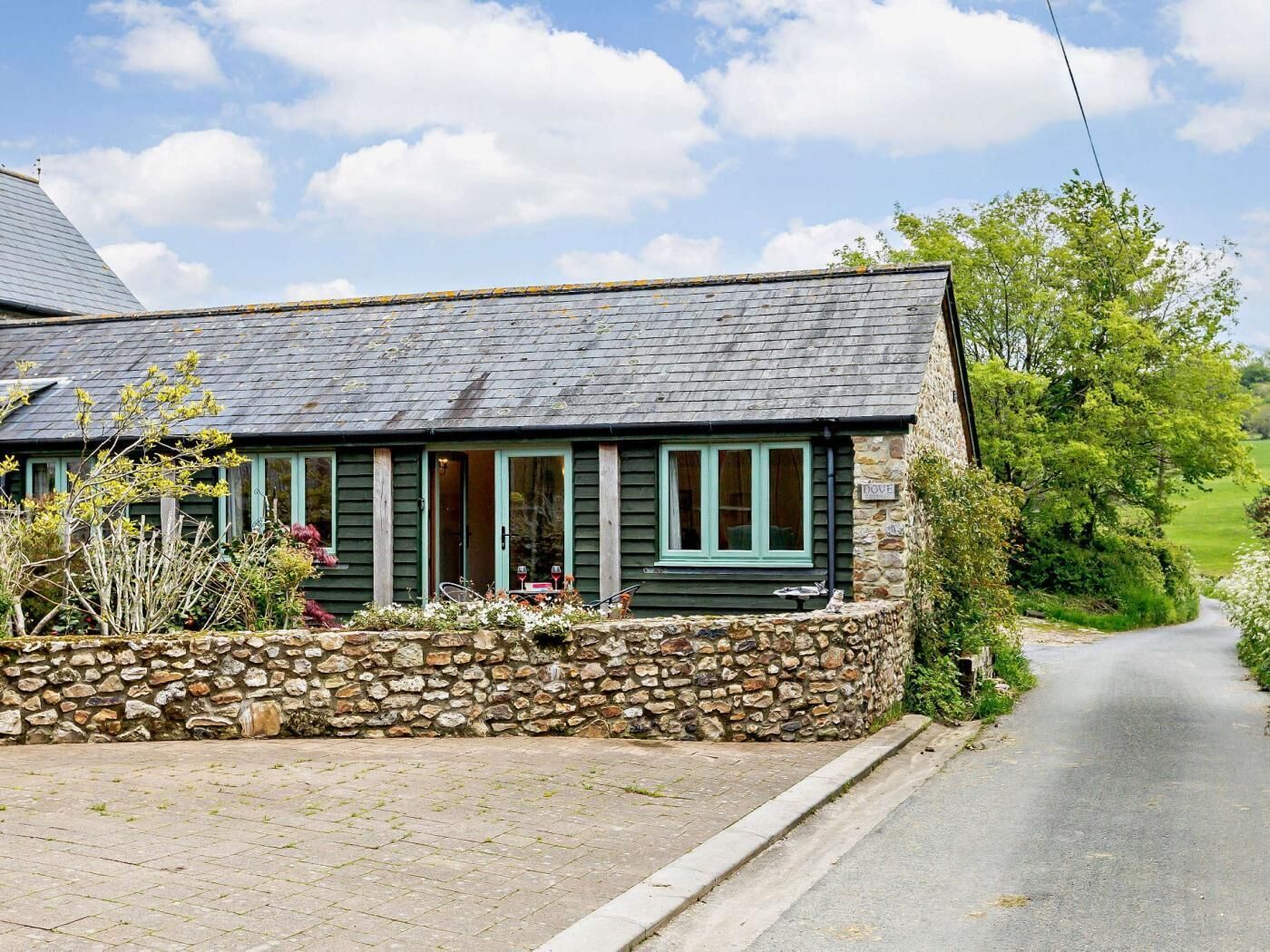 A stone-walled cottage with a slate roof, a stone pathway leading to the entrance, and a sign indicating the name 'DOVE.'