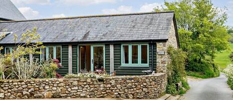A stone-walled cottage with a slate roof, a stone pathway leading to the entrance, and a sign indicating the name 'DOVE.'