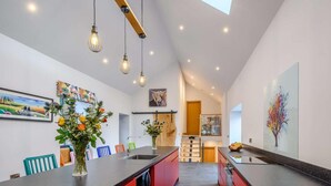 Una cocina moderna con una isla central, iluminación colgante y una escalera que conduce a una zona tipo loft.