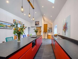 Eine moderne Küche mit einer zentralen Kochinsel, Pendelleuchten und einer Treppe, die zu einem Erkerraum führt.