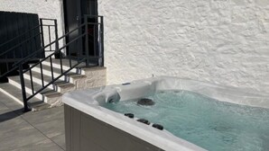 Un jacuzzi con revestimiento de piedra, una escalera de metal y una pared blanca.