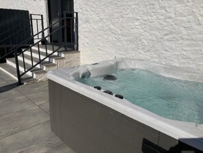 Ein Whirlpool mit Steinverkleidung, einer Metalltreppe und einer weißen Wand.
