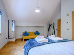 Ein Schlafzimmer mit einem Bett, einem gelben Sofa, einer Hängelampe und einer Tür.