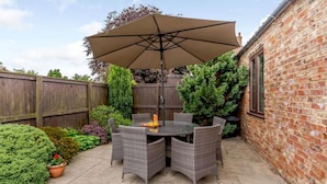 A patio with a round table and chairs, a large umbrella, and a brick wall. - 3 Bed in York (oc-83264) (High Catton)