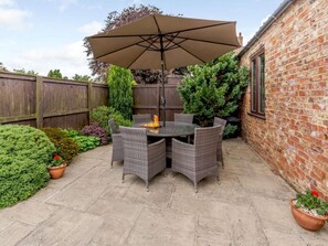 Eine Terrasse mit rundem Tisch und Stühlen, einem großen Sonnenschirm und einer Backsteinmauer.