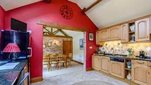 A kitchen with wooden cabinets, a red wall, a clock, and a dining area with chairs. - 3 Bed in York (oc-83264) (High Catton)
