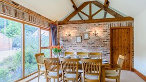 A dining room with a brick wall, wooden beams, a large window, and a table set for six. - 3 Bed in York (oc-83264) (High Catton)