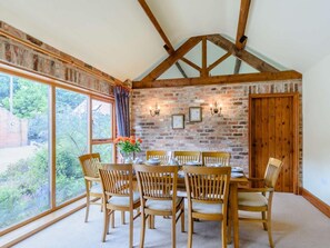 Ein Esszimmer mit Backsteinwand, Holzbalken, einem großen Fenster und einem Tisch, gedeckt für sechs Personen.