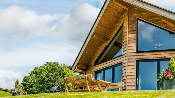 Een moderne houten hut met een groot raam, een eethoek met tafel en stoelen, en een tuin met bomen en bloemen.