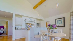 Een moderne keuken met witte kasten, een eetgedeelte met een ronde tafel en witte stoelen, en een zichtbare klok aan de muur.