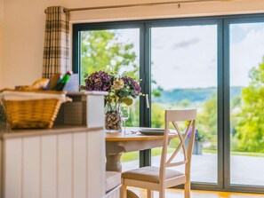 Spiseområde med bord, stole og udsigt gennem store vinduer.