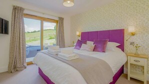 Een slaapkamer met een groot bed, uitzicht, een paars hoofdeinde en een nachtkastje met een lamp.