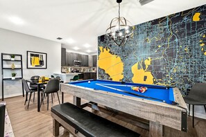 Una mesa de billar con un mural de un mapa de la ciudad, un comedor con sillas y una mesa, y una cocina al fondo.