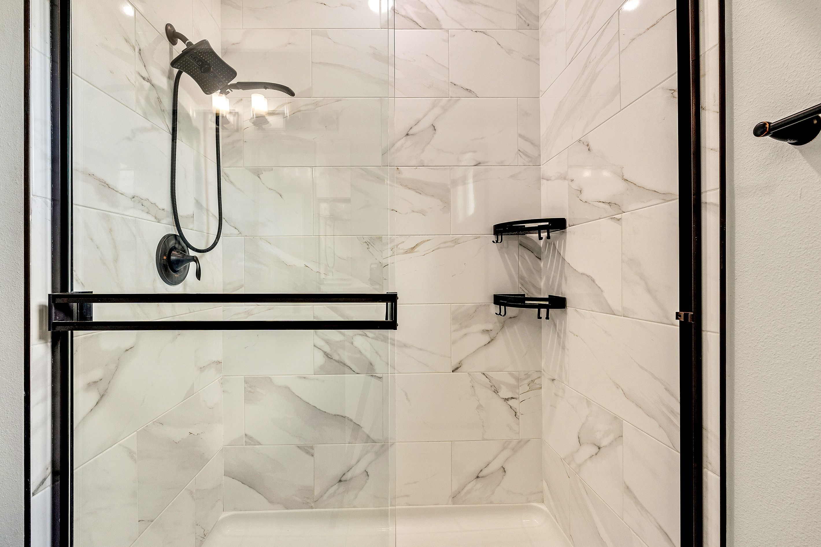 A modern shower area with a glass enclosure, a handheld showerhead, and a wall-mounted faucet.
