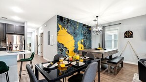 Een moderne keuken met een centraal eiland, een eethoek met stoelen en een gedekte tafel, en een groot abstract wandkunstwerk.