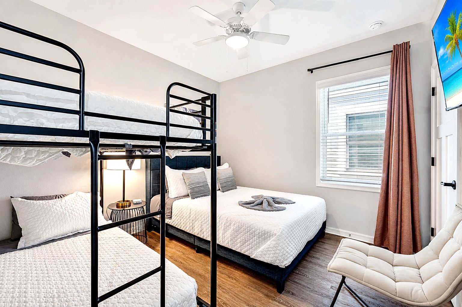 A hotel room with bunk beds, a ceiling fan, a window with blinds, and a chair.