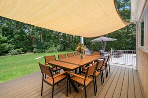 An outdoor patio with a wooden table and chairs, a canopy, and a grill. - New Construction Designer Home: Private Outdoor Oasis, Hot Tub, Sauna (Eastham)