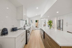 Une cuisine moderne avec des meubles blancs, des appareils électroménagers en acier inoxydable et un plancher en bois.