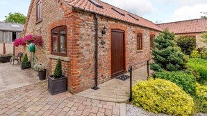 A brick building with a red-tiled roof, a wooden door, and a small porch area with potted plants. - 1 Bed in York (oc-83265) (High Catton)