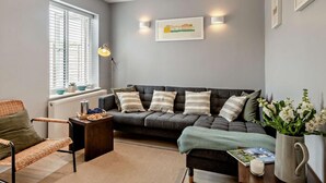 Een woonkamer met een bank, een stoel, een salontafel en een raam met zonwering.