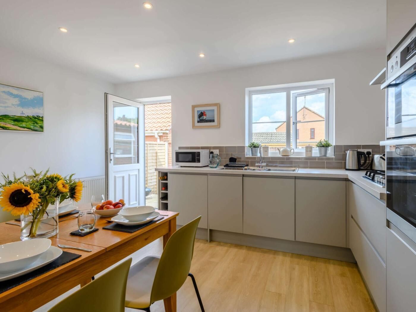 Een moderne keuken met witte kastjes, een magnetron en een kookplaat. Er is een zithoek met een houten tafel en stoelen.