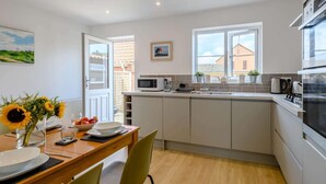 Een moderne keuken met witte kastjes, een magnetron en een kookplaat. Er is een zithoek met een houten tafel en stoelen.