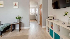Een moderne woonkamer met een bank, een salontafel, een aan de muur bevestigde televisie en een boekenplank.