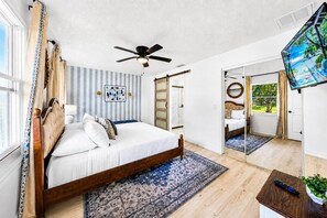 Une chambre à coucher avec un lit, un ventilateur de plafond, une télévision et un grand miroir.