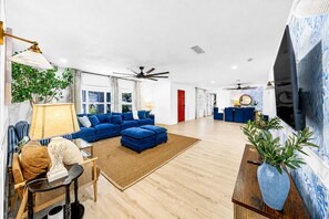 Un salon spacieux avec un canapé d’angle bleu, une table basse en bois et un téléviseur fixé au mur.