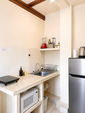 A compact kitchen with a sink, a microwave, a stainless steel refrigerator, a built-in induction cooktop, and a small countertop with a blender and other items. - Apartment 6 | Casa Maakja (Ixmiquilpan)