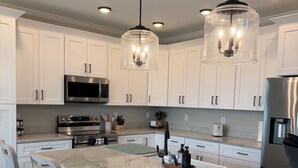 Una cocina moderna con gabinetes blancos, electrodomésticos de acero inoxidable, una isla de mármol e iluminación colgante.