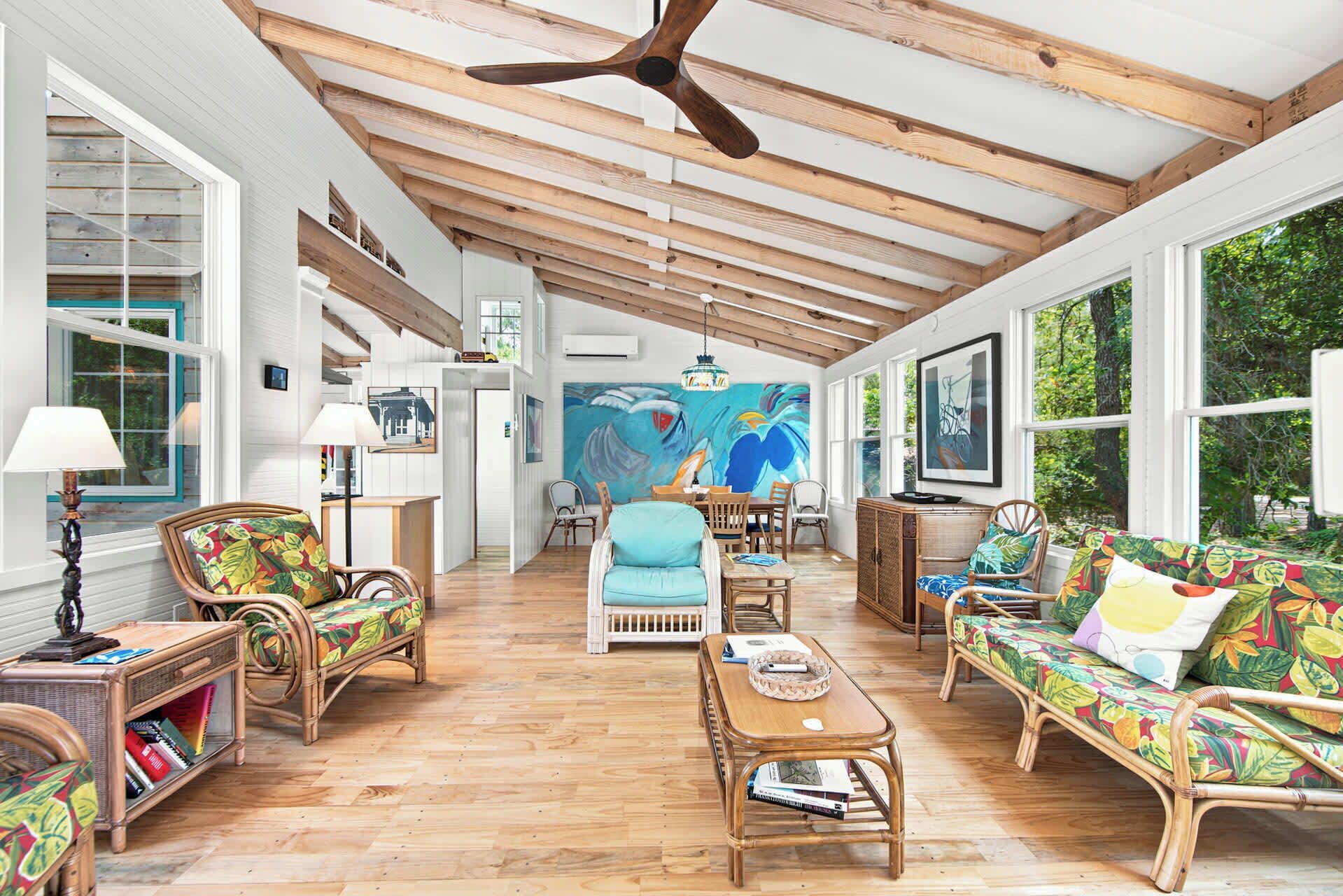 A spacious room with wooden beams, a dining area, and a large window with a view of greenery.