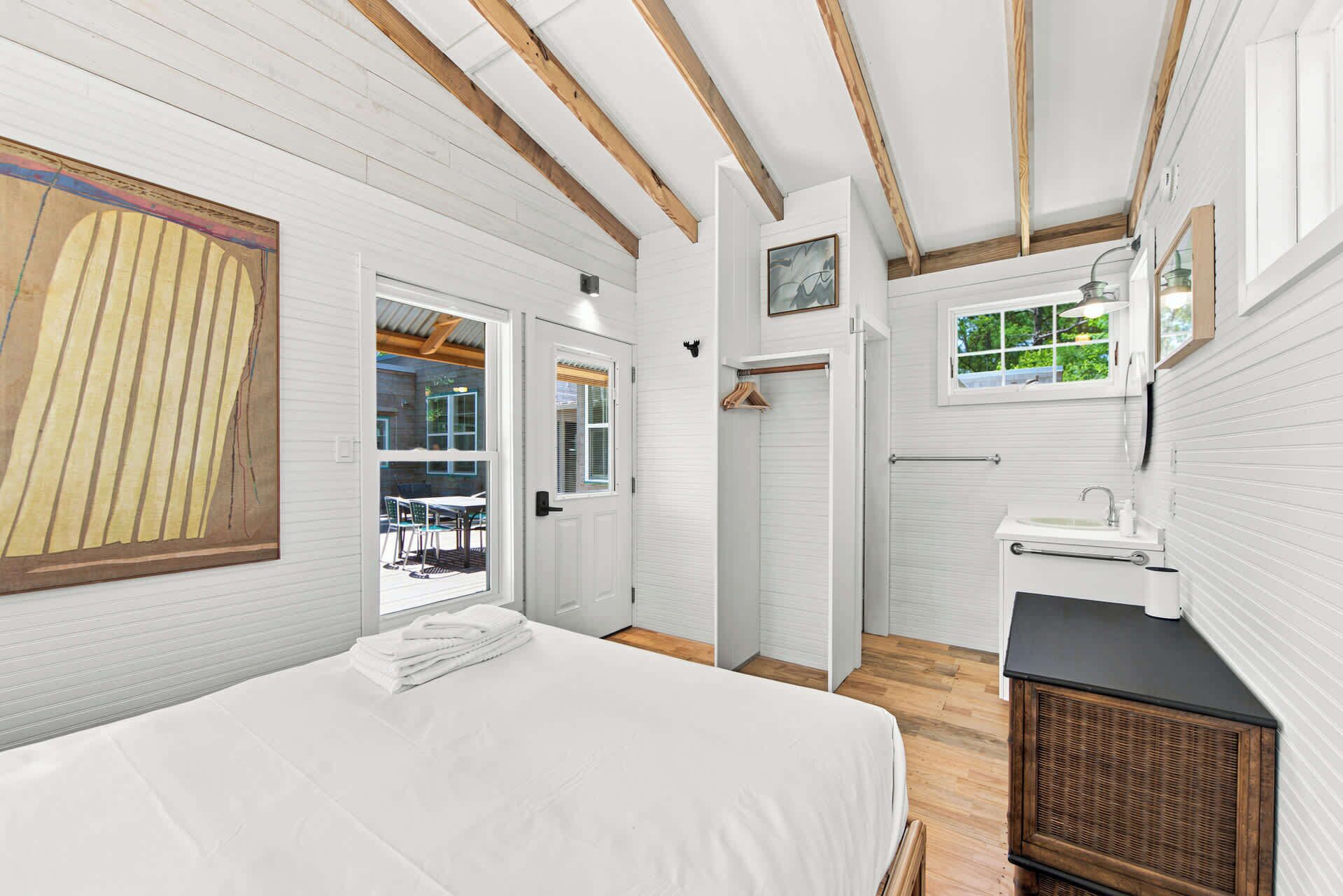 Un dormitorio con cama, ventana, puerta y baño con lavamanos y espejo.