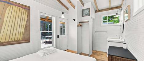 Un dormitorio con cama, ventana, puerta y baño con lavamanos y espejo.