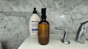 A bathroom with a marble backsplash, a white bottle of Aveeno lotion, and a brown bottle with a pump dispenser.