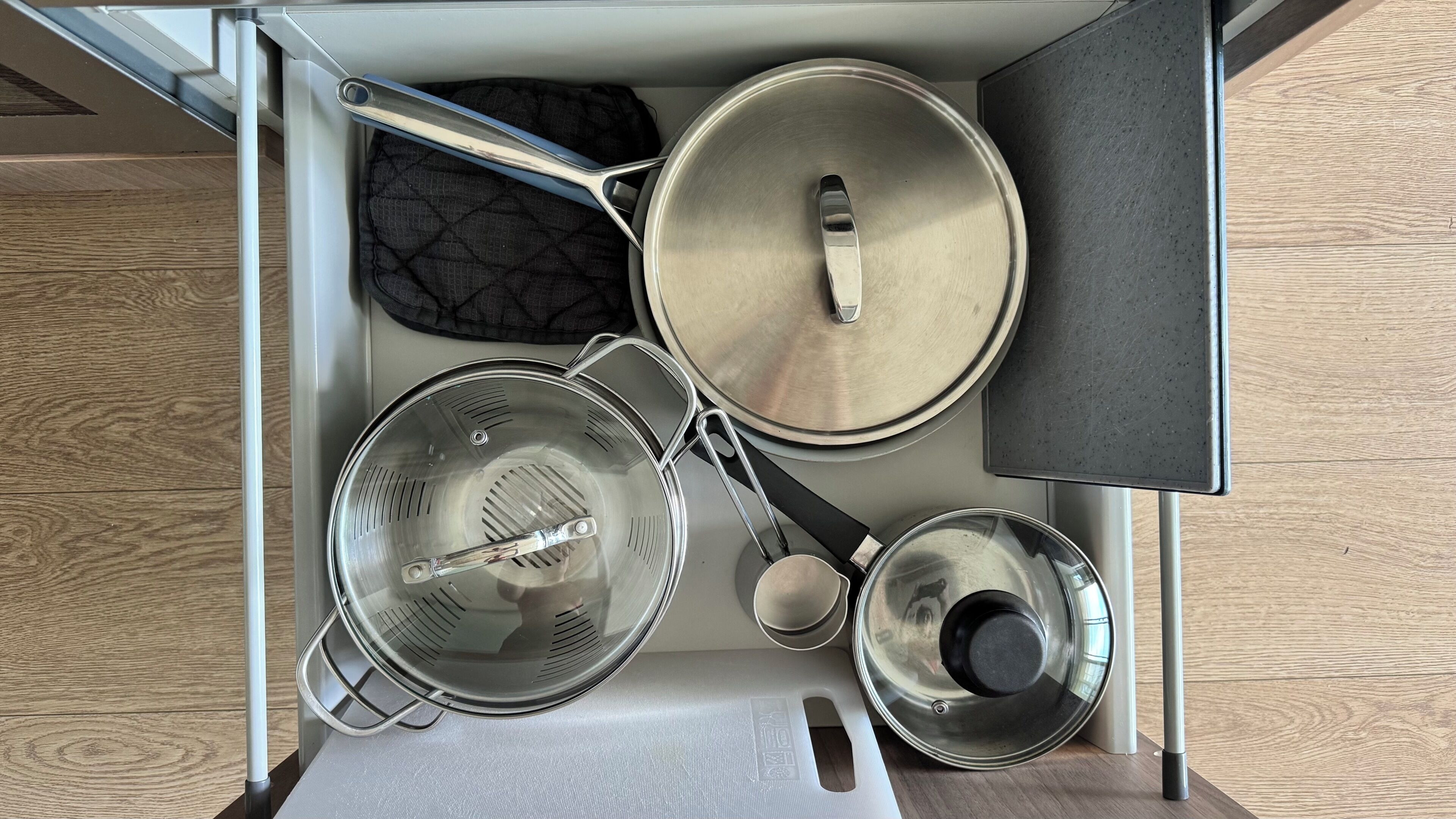 Un cajón de cocina con diversos utensilios de cocina, incluyendo ollas, un colador y una cuchara para servir.