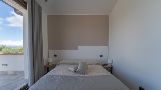 A modern hotel room with a large bed, two bedside tables with lamps, a view of the outdoors, and a simple, clean design. - Villa Quattro Lune - Partinico (Partinico)