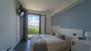 A modern hotel room with a large bed, a bedside table with a lamp, a TV mounted on the wall, and a balcony with a view of greenery. - Villa Quattro Lune - Partinico (Partinico)