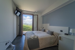 A modern hotel room with a large bed, a bedside table with a lamp, a TV mounted on the wall, and a balcony with a view of greenery. - Villa Quattro Lune - Partinico (Partinico)