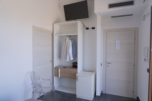 Een kamer met een garderobe, een bureau, een stoel en een aan de muur bevestigde televisie.