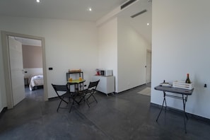 A modern hotel room with a bed, a dining table with chairs, a small kitchenette, and a desk with a chair. - Villa Quattro Lune - Partinico (Partinico)