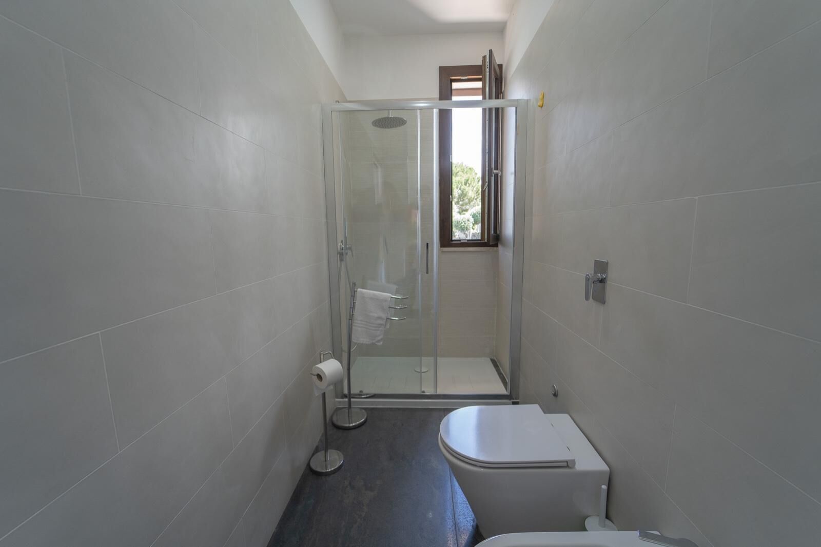 A small bathroom with a toilet, a glass shower enclosure, and a window.