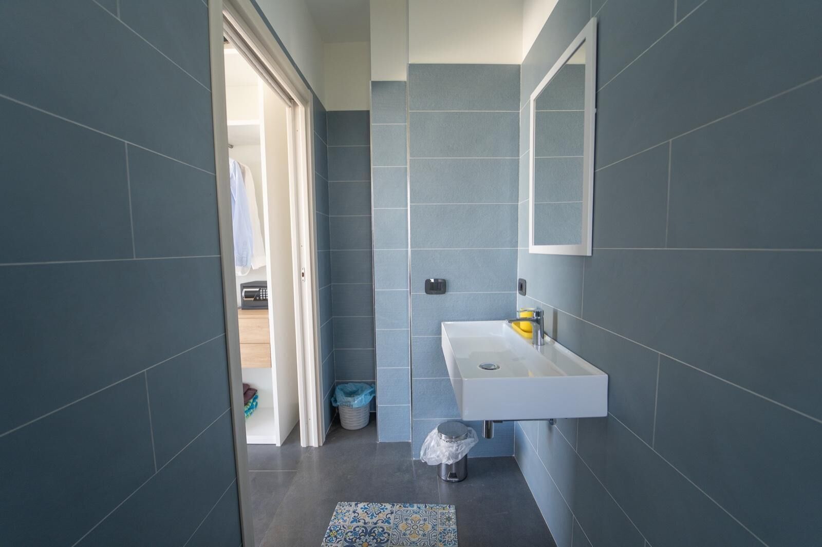 A bathroom with a white sink, blue tiles, a mirror, and a patterned rug.