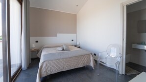 A modern bedroom with a bed, bedside tables, a chair, and a bathroom with a sink and mirror. - Camera Luna Perla - Partinico (Monreale)