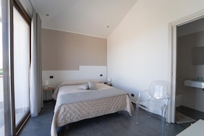 A modern bedroom with a bed, bedside tables, a chair, and a bathroom with a sink and mirror.