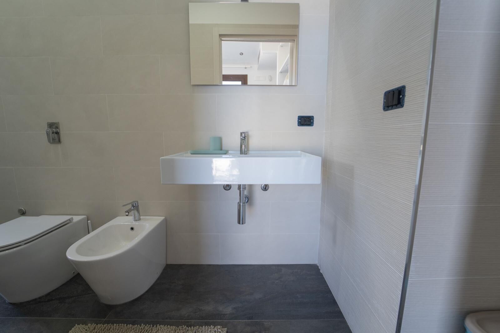 Et badeværelse med en hvid vask, en bidet og et spejl over vasken.