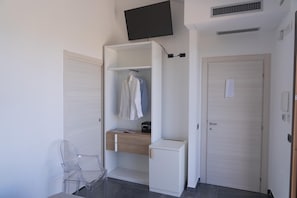 A room with a wardrobe, a desk, a chair, and a television mounted on the wall.