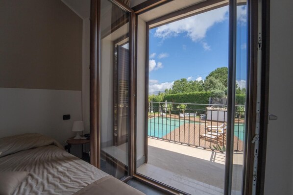 A bedroom with a large sliding glass door leading to a balcony with a pool.