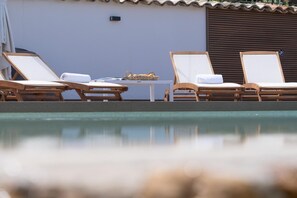 Zona de piscina amb gandules de fusta, una taula petita amb una cistella, i una paret amb el símbol de número.